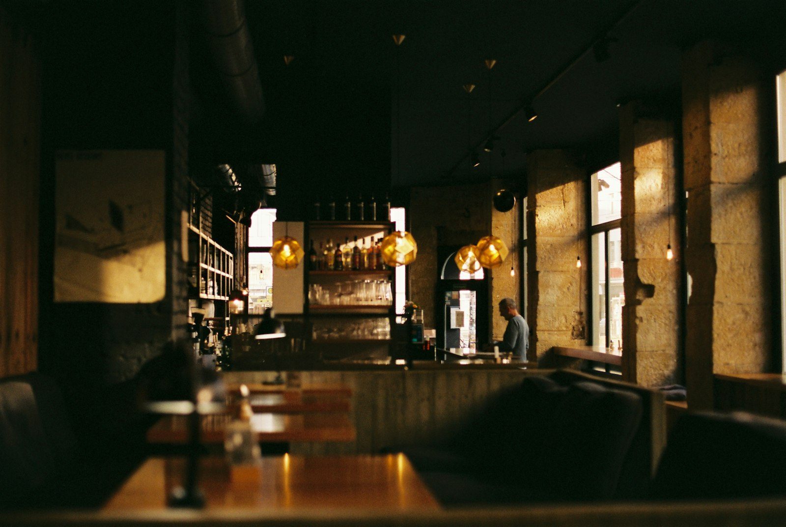 Moderne Website für ein Restaurant, Beispielansicht: Gastraum in warmem Licht, goldene Hängelampen über der Bar, Holztische und Steinwände